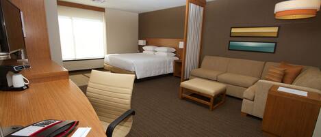 A hotel room with a bed, a sofa, a desk with a computer, a chair, and a coffee maker.