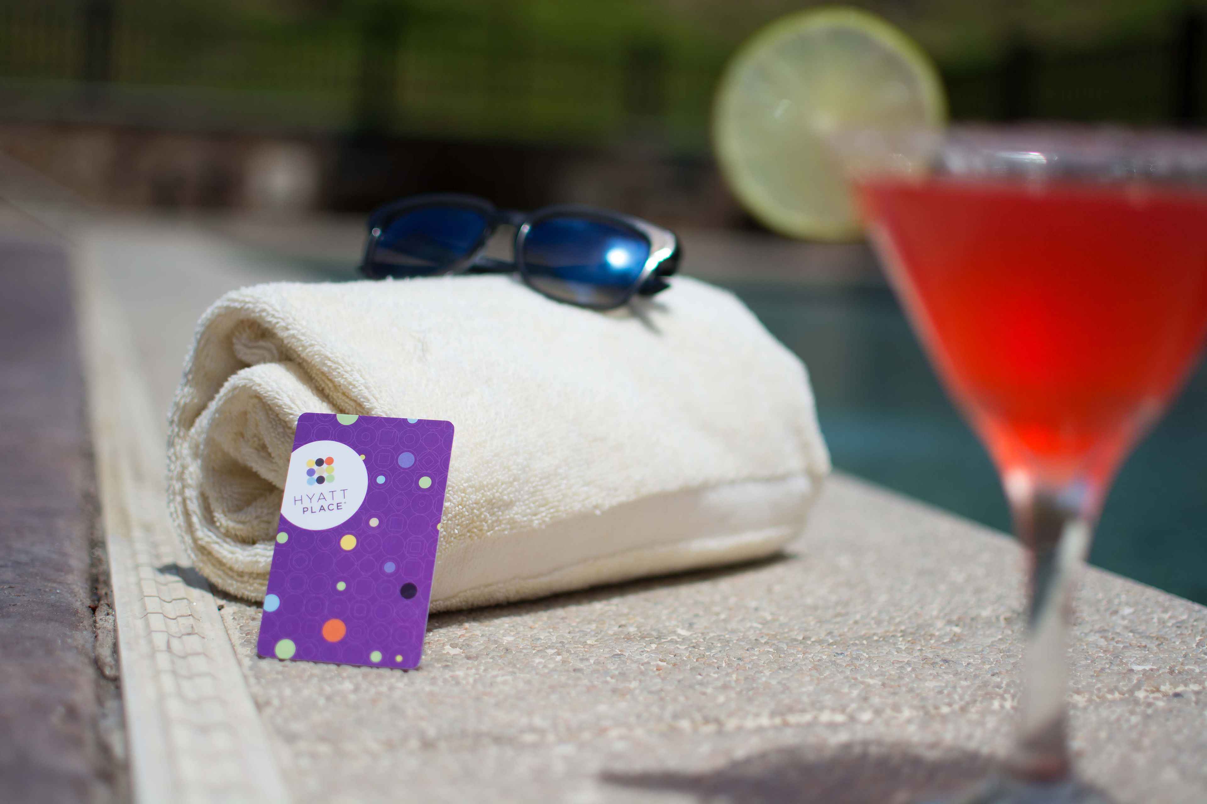 A towel with a tag, sunglasses, and a cocktail glass by a pool.