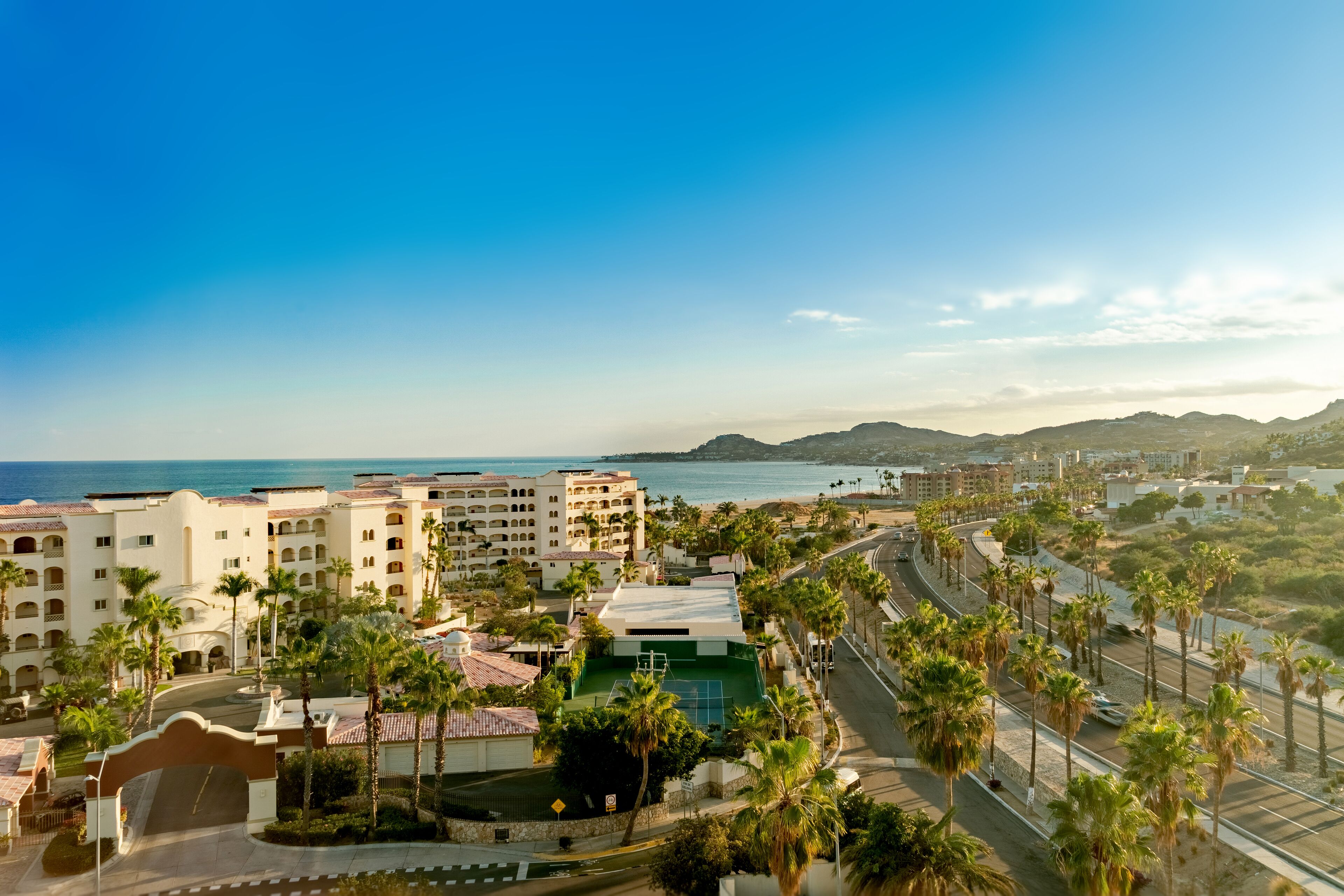 Un resort con varias construcciones, palmeras y un camino que lleva a la playa.