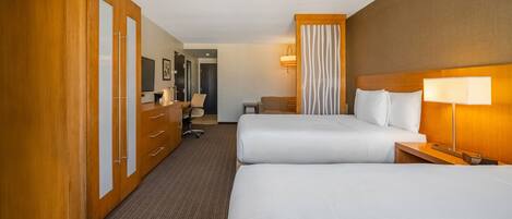 Habitación de hotel con dos camas, armario de madera, escritorio, silla, lámpara y vista al pasillo.