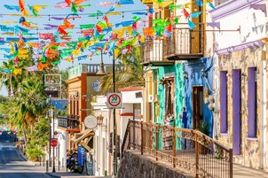 Rua com bandeiras coloridas, uma farmácia e placa de limite de velocidade.