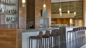 A modern bar area with multiple stools, a bar counter, and shelves displaying bottles. - Hyatt Place Los Cabos (San José del Cabo)