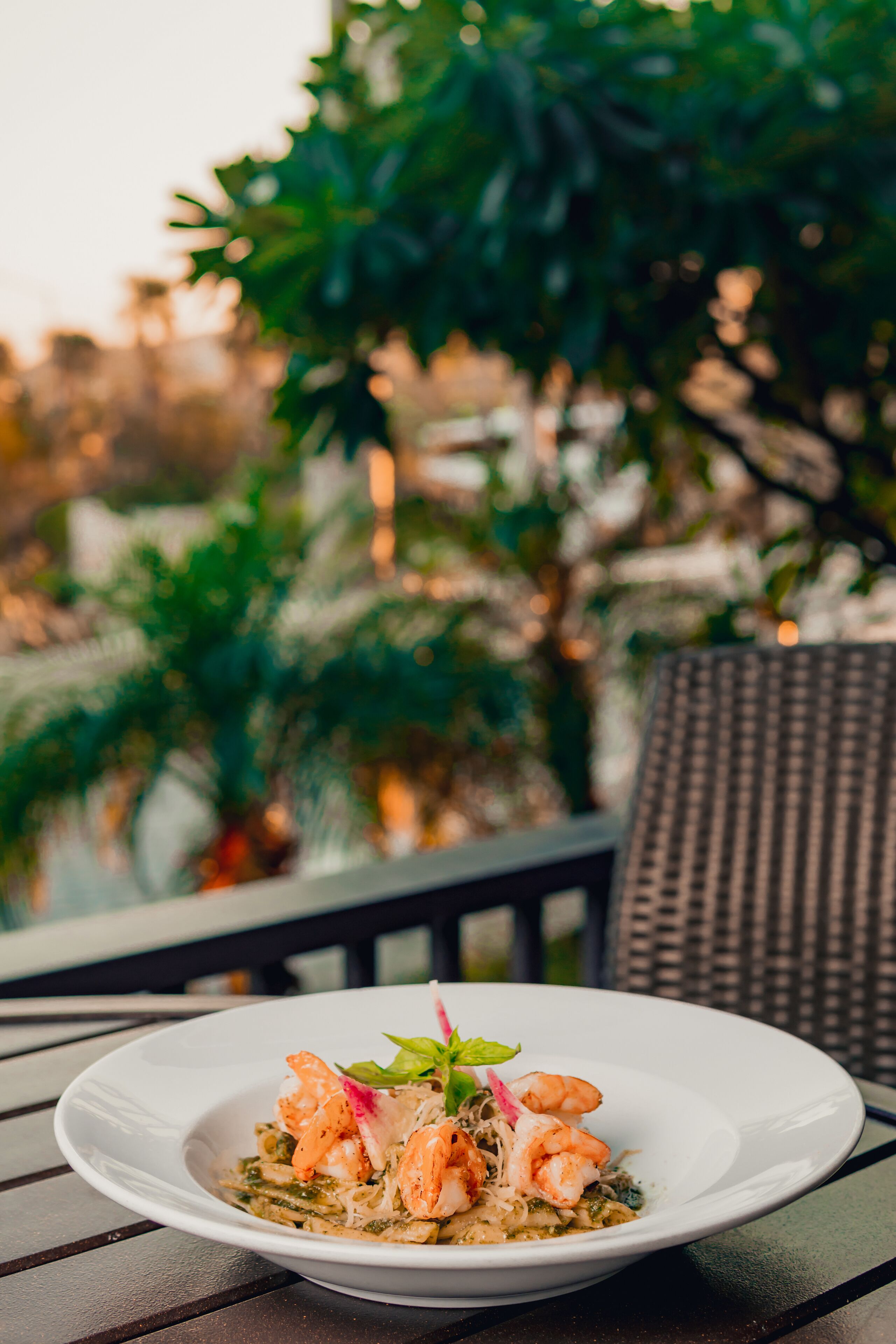 Une assiette blanche contenant des crevettes et des pâtes, posée sur une table, avec une chaise en osier en arrière-plan.