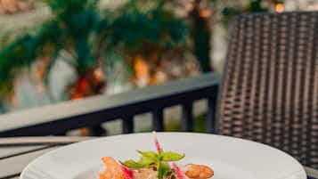 Une assiette blanche contenant des crevettes et des pâtes, posée sur une table, avec une chaise en osier en arrière-plan.