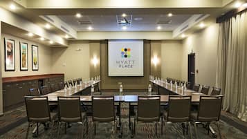 Une salle de conférence avec une longue table, des chaises et un écran de projection affichant le logo de Hyatt Place.