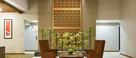 Un vestíbulo con mostrador de recepción, dos sillones, una mesa de centro, un panel decorativo y un arreglo de plantas.
