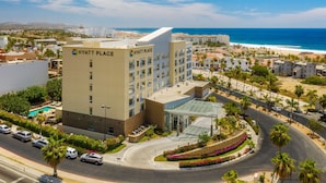A multi-story hotel with a pool, surrounded by palm trees and a beach view. - Hyatt Place Los Cabos (San José del Cabo)