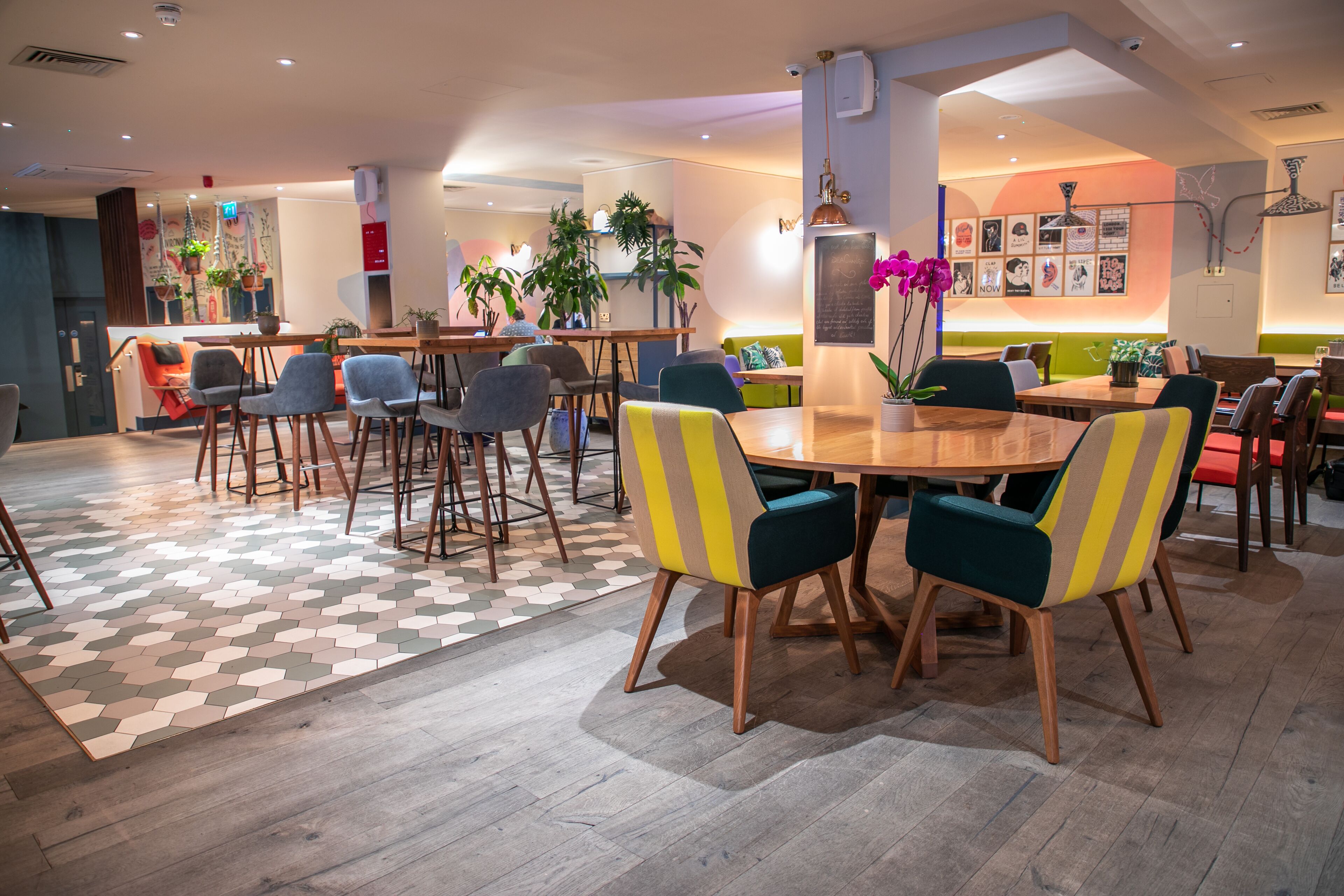 A modern dining area with wooden tables and chairs, a patterned floor, and potted plants.