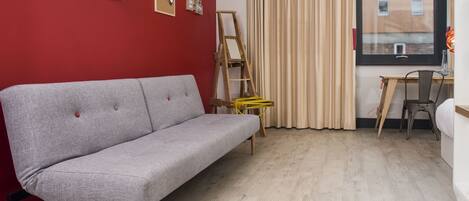 A room with a grey sofa, a wooden ladder, a small table, and a window with curtains.