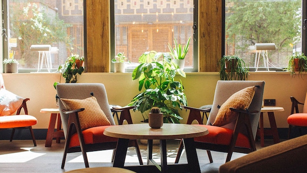 A cozy seating area with two chairs and a table, surrounded by potted plants and a large window with a view of greenery. - The Corner London City (London)