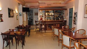 Un bar d’hôtel avec des tables et des chaises en bois, un comptoir bien garni de bouteilles et un téléviseur fixé au mur.