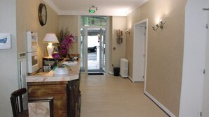 Un hall d’hôtel comprenant un comptoir d’accueil, un réfrigérateur, une lampe et un vase avec des fleurs.