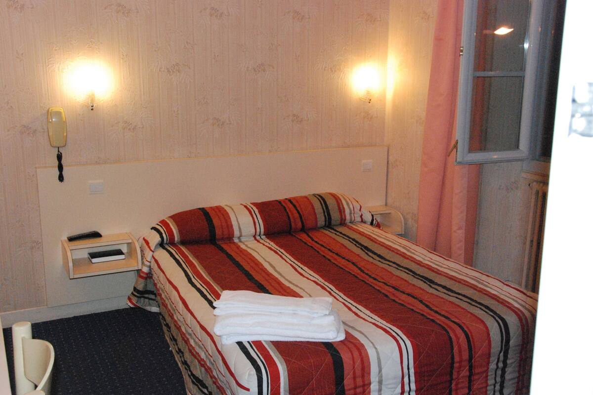A hotel room with a bed, a nightstand, a lamp, and a telephone.