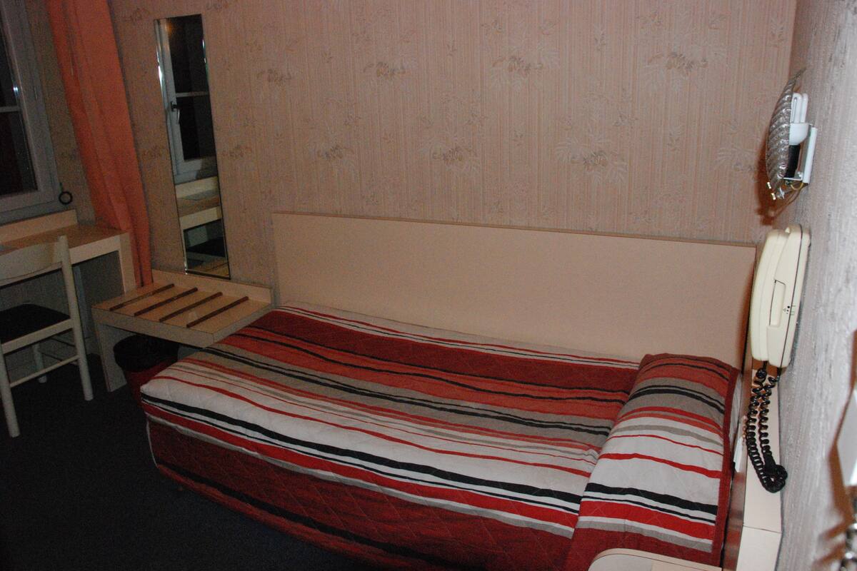 A single bed with a striped blanket, a bedside table, a mirror, and a telephone.