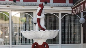 Une fontaine ornée d’une statue blanche et d’un socle rouge, située devant un bâtiment sur lequel on peut lire l’inscription « RESTAURANT A ».