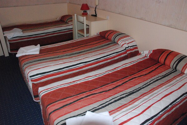 Une chambre d’hôtel avec deux lits, chacun doté de draps à rayures, une petite table avec une lampe et un téléphone fixé au mur.