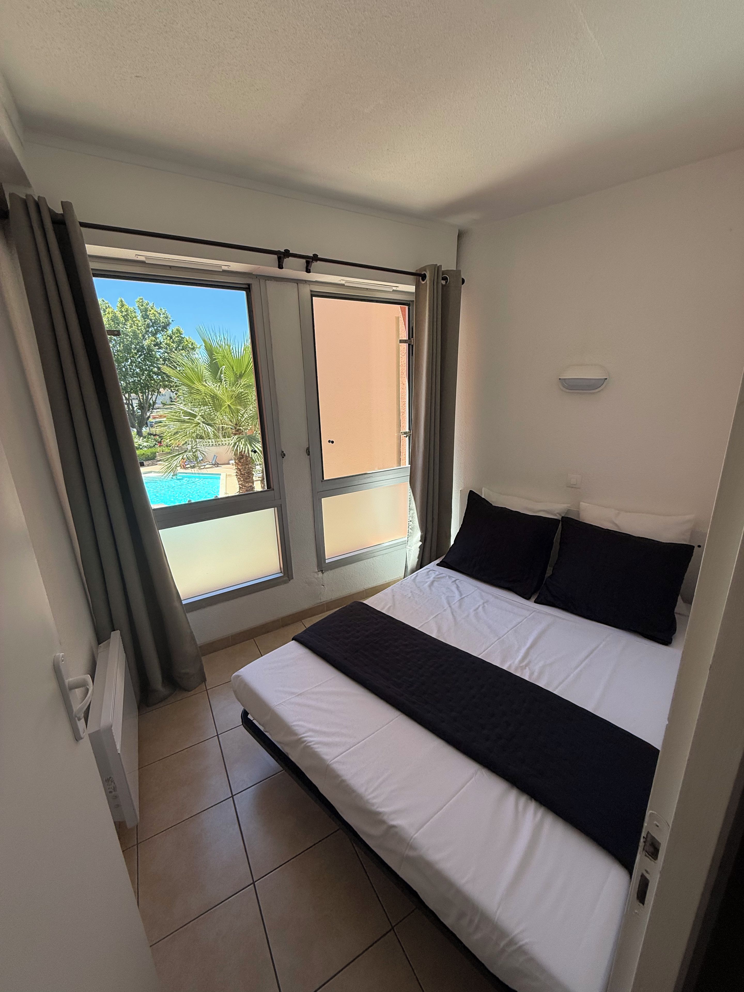 A bedroom with a bed, a window, and a view of a swimming pool.