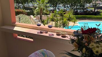 En balkon med udsigt til en swimmingpool, et bord med en vase blomster og et håndklæde.