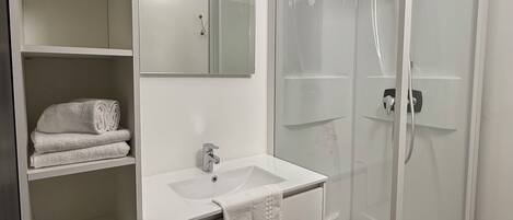 Un baño con lavamanos blanco, espejo y cabina de ducha con paredes de vidrio.