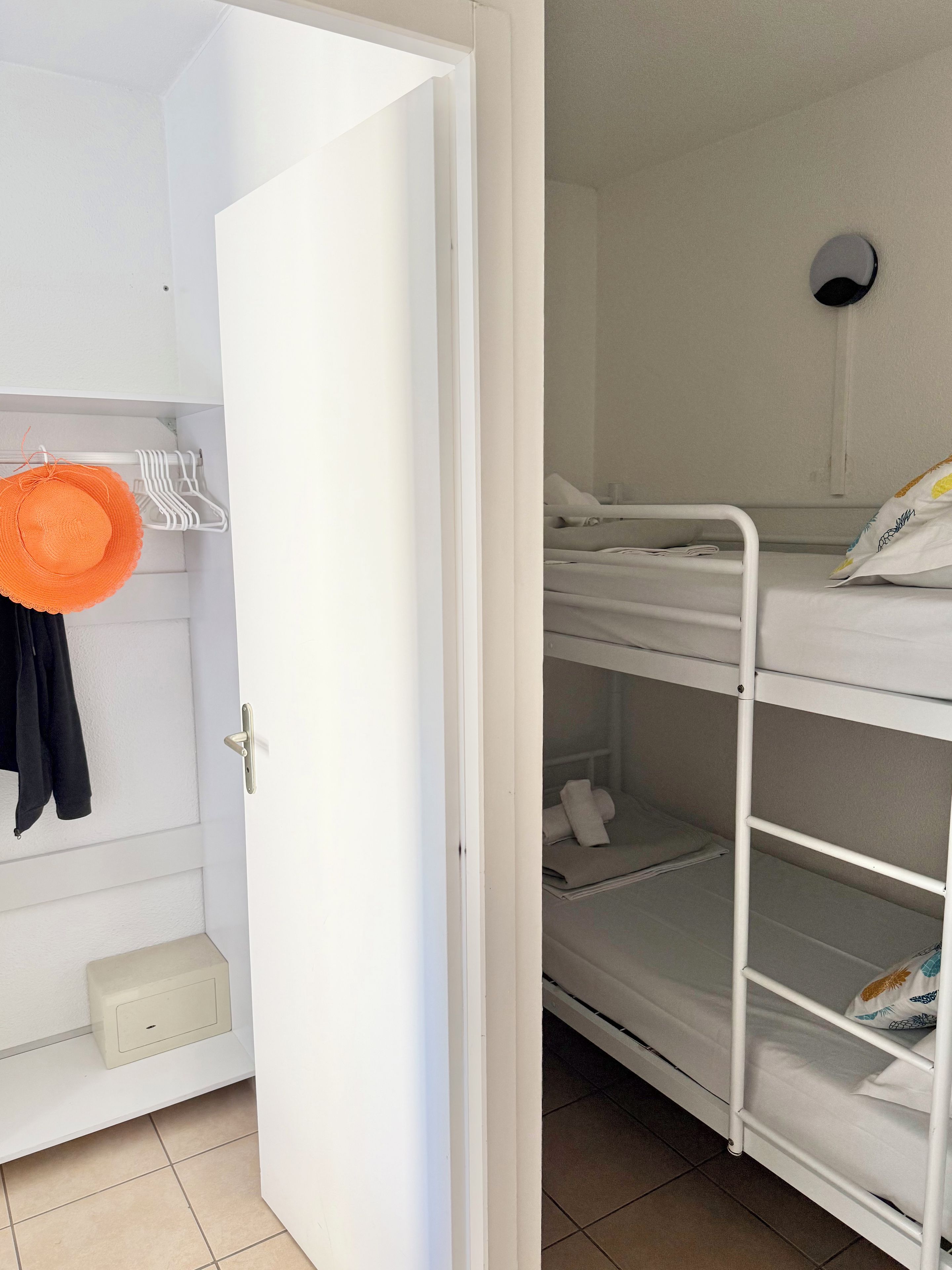 Una habitación con una cama litera, una puerta blanca y un estante con un sombrero y una chaqueta.