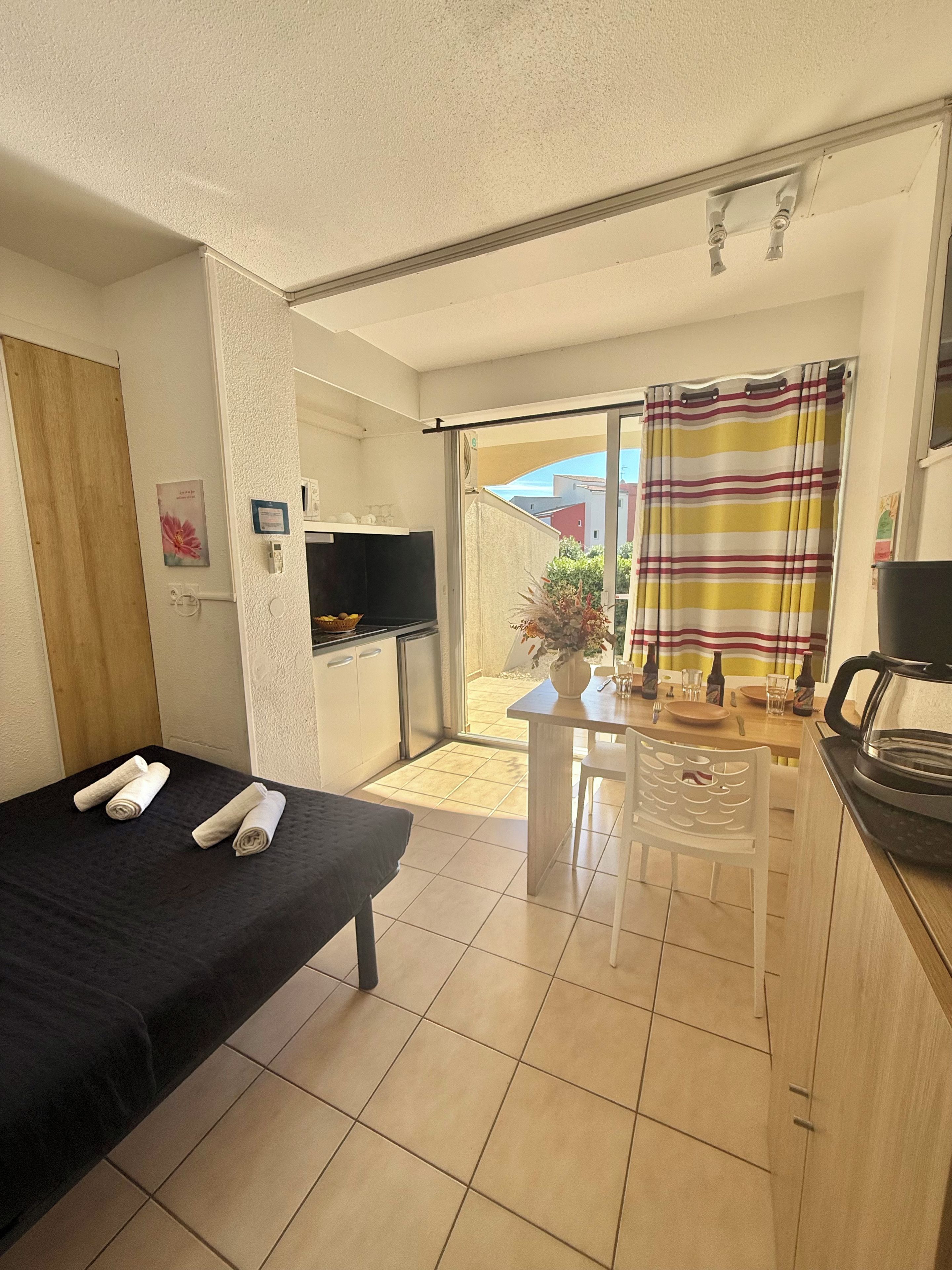 A room with a bed, a small table, a TV, and a view of the outside.
