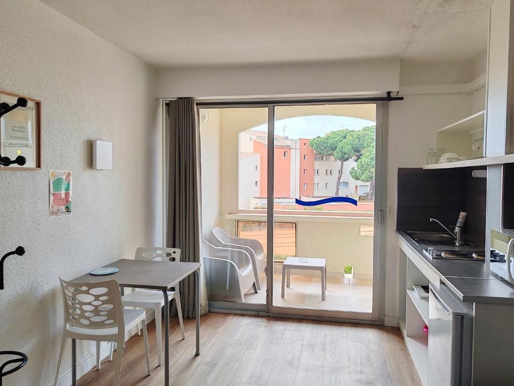 Quarto compacto com porta de vidro deslizante para uma varanda, uma pequena mesa de jantar e uma área de cozinha compacta.