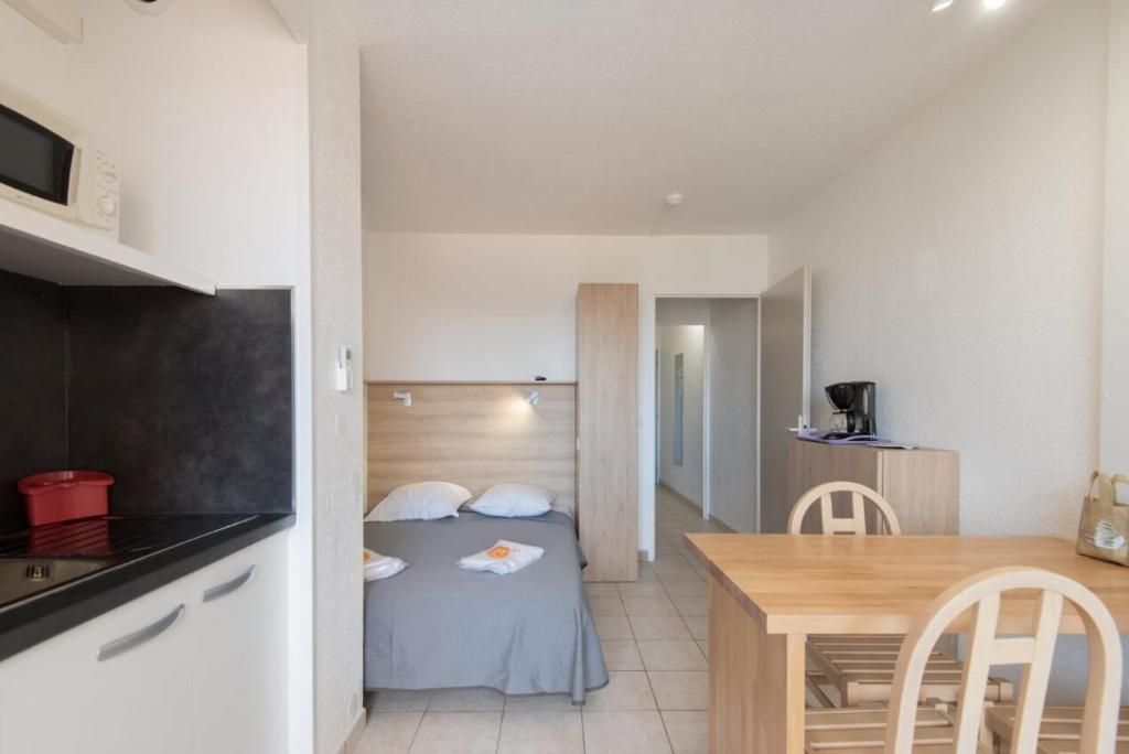 A compact room with a bed, a small kitchenette, a dining table, and a chair.