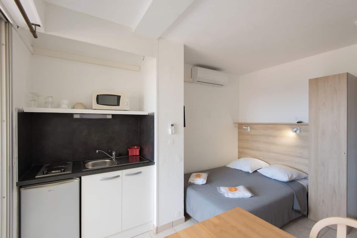 Una habitación compacta con kitchenette, una cama, una mesita y una silla.