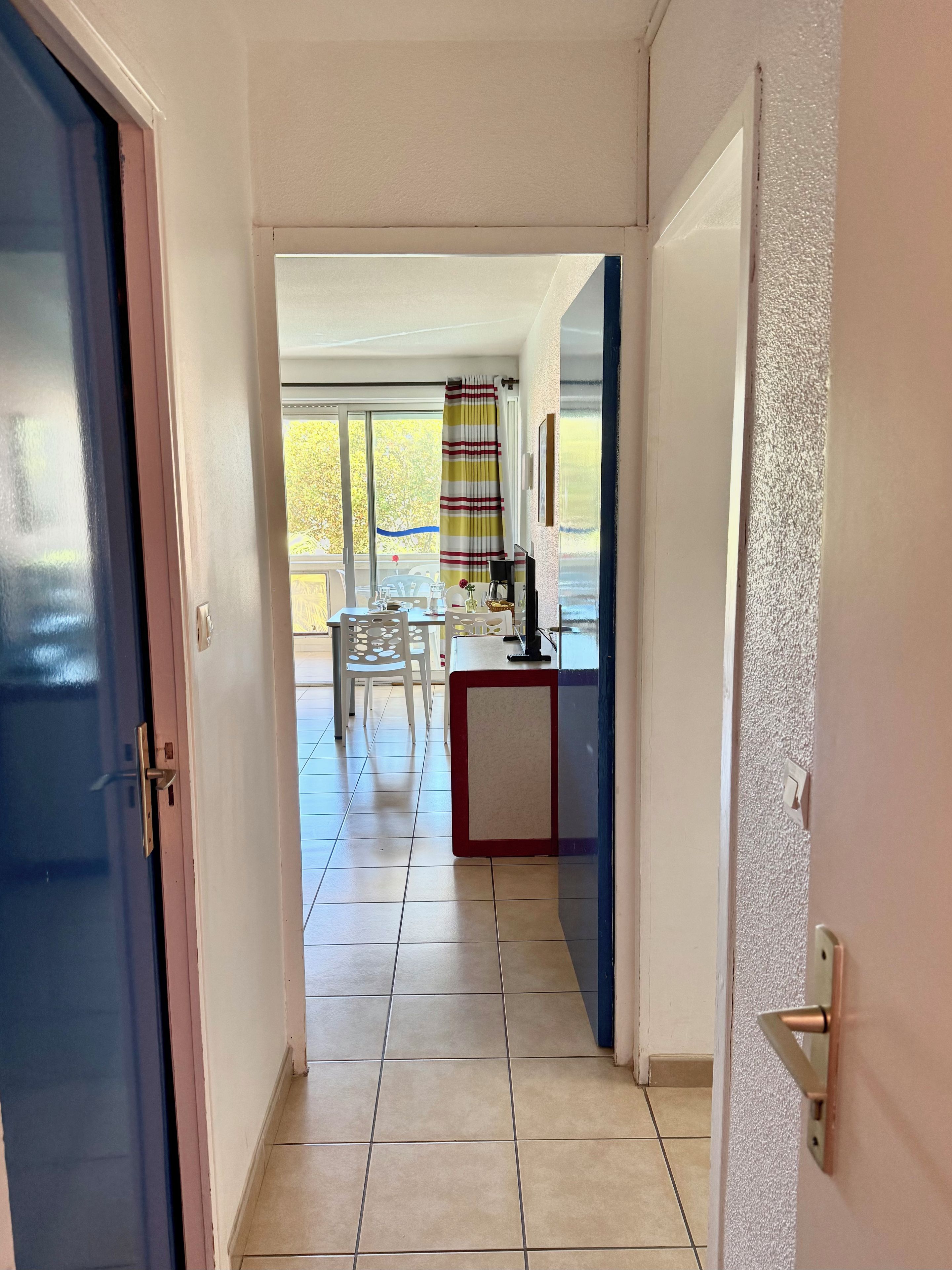 Un couloir mène à une salle à manger équipée d’une table et de chaises, d’un petit comptoir et offrant une vue sur l’extérieur.