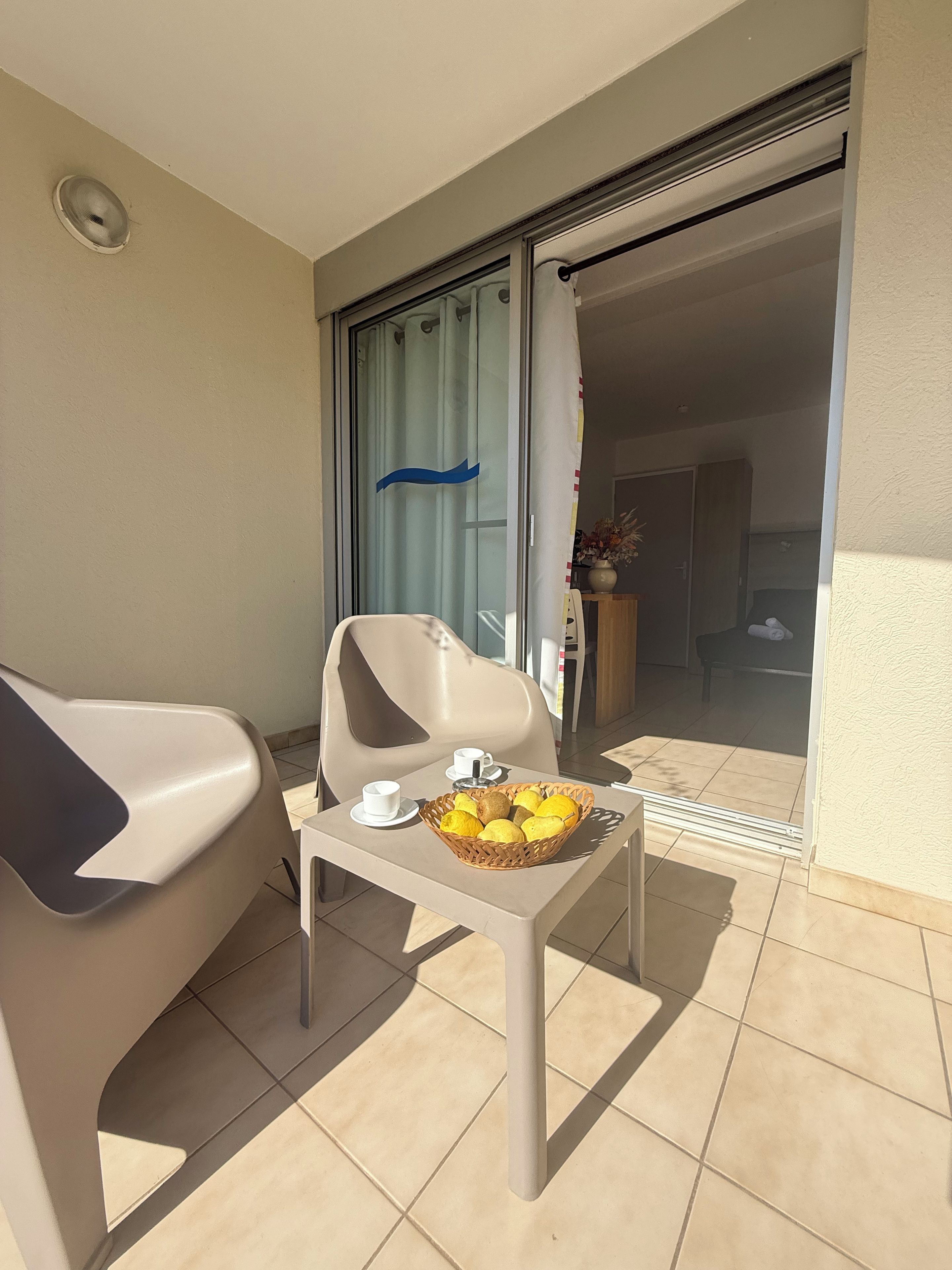 A balcony with a table, a chair, a basket of fruit, and a sliding glass door.