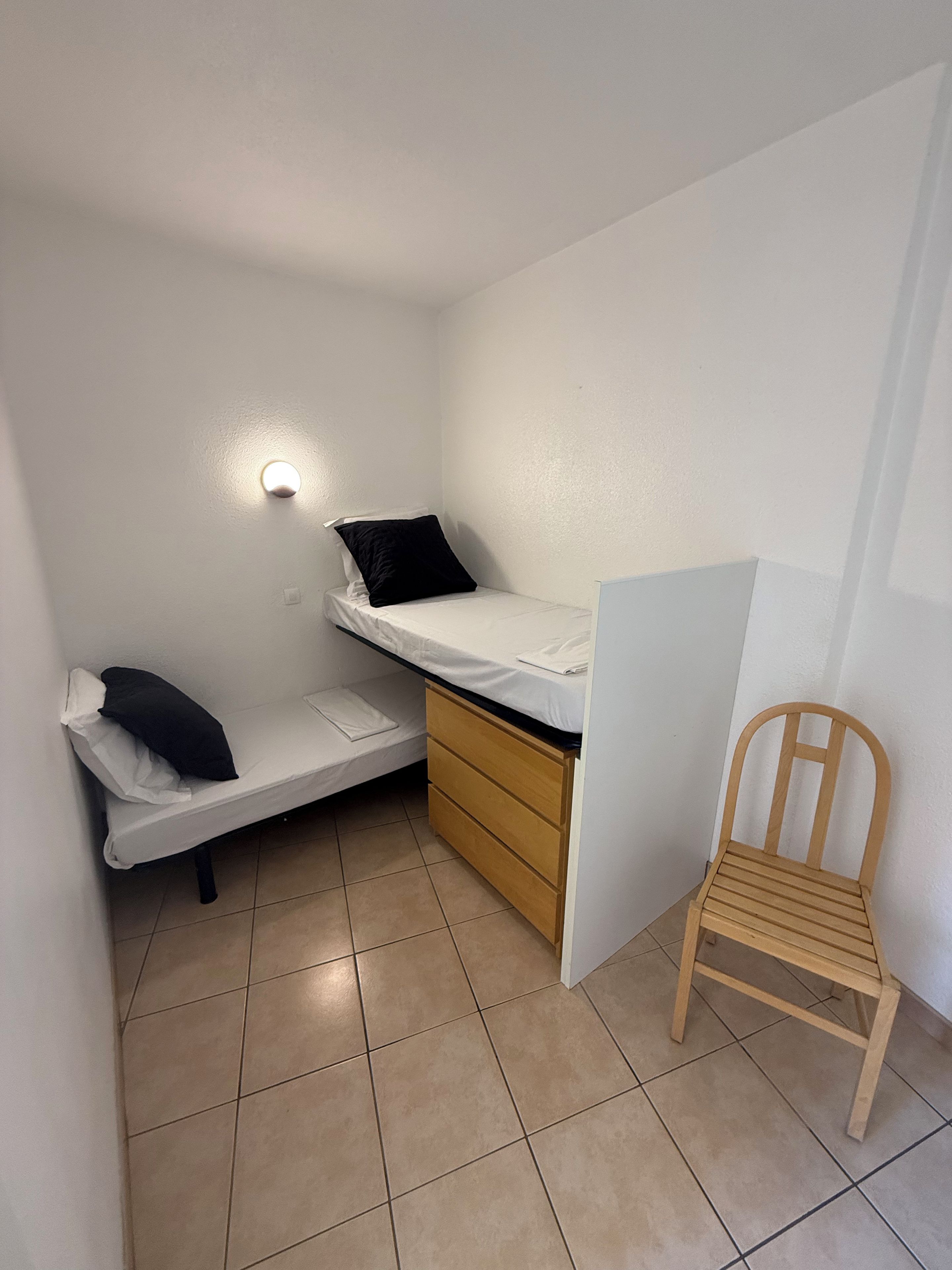 A small, compact room with a bed, a desk, and a chair.