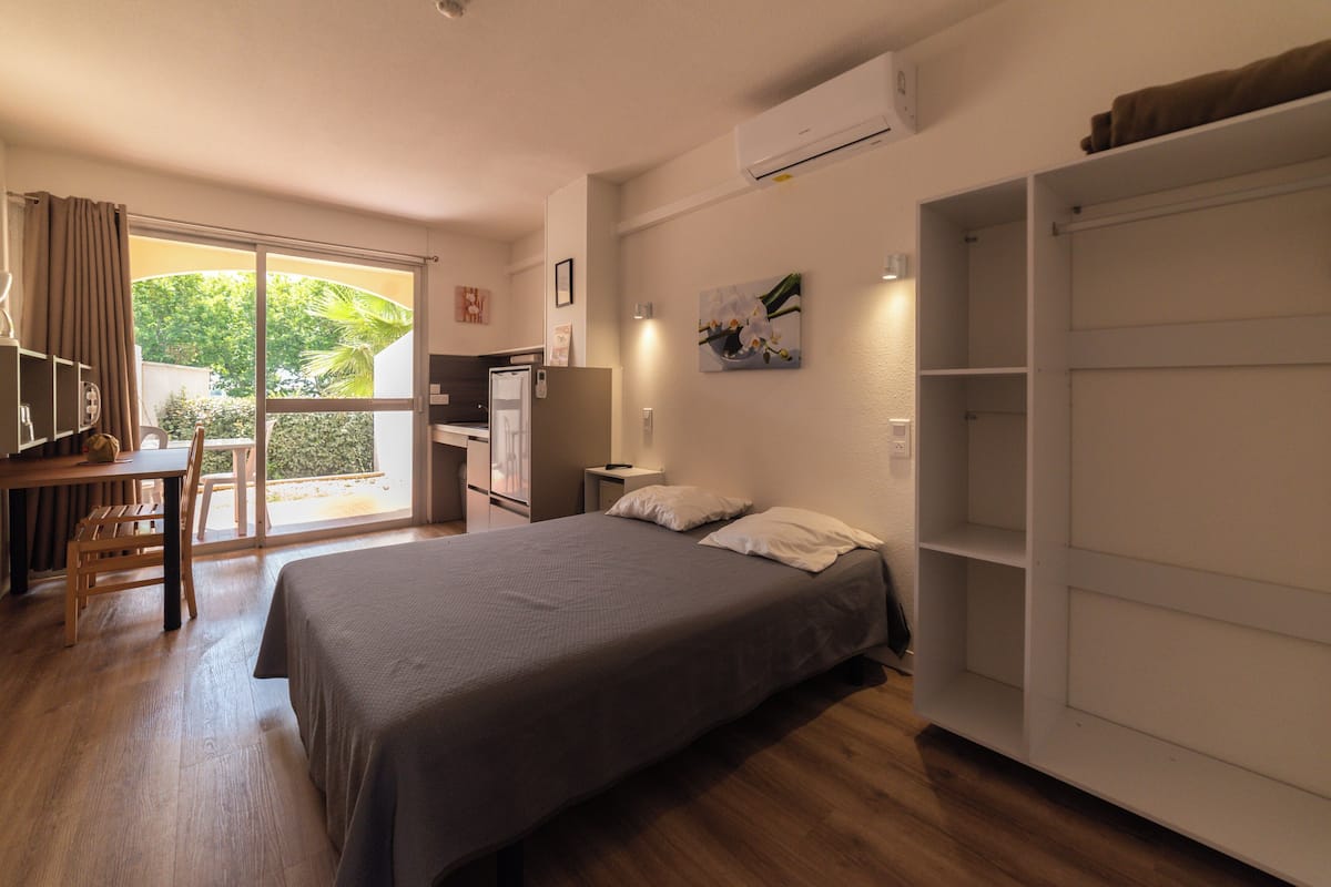 Un dormitorio con cama, escritorio, silla, armario y puerta corrediza a un balcón.