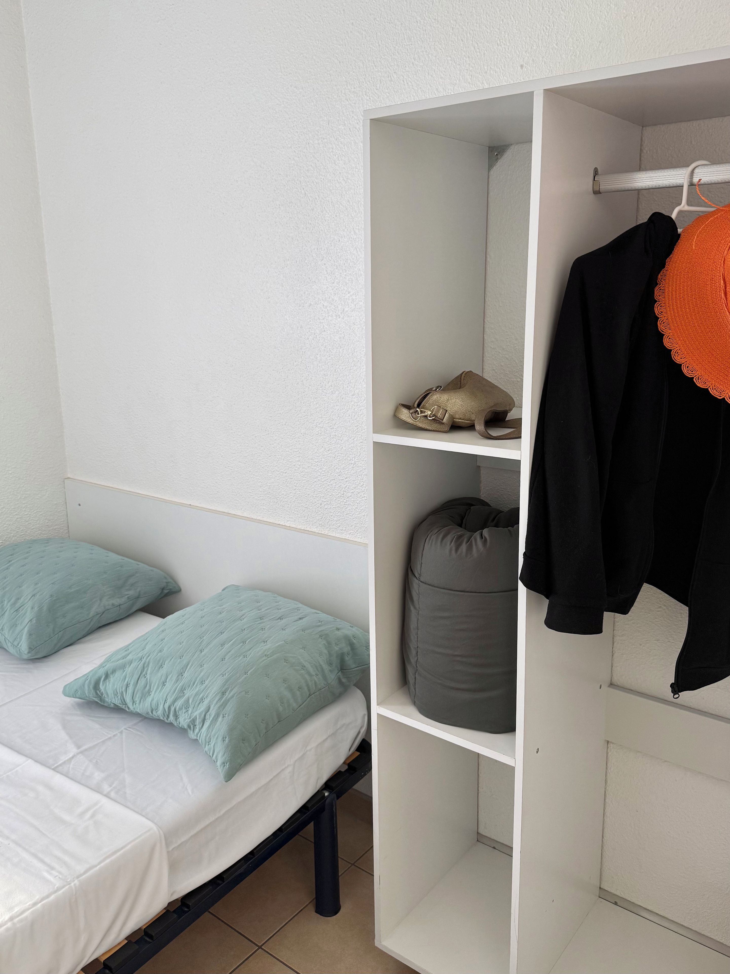 A bedroom with a bed, pillows, a wardrobe, and a hanging garment.