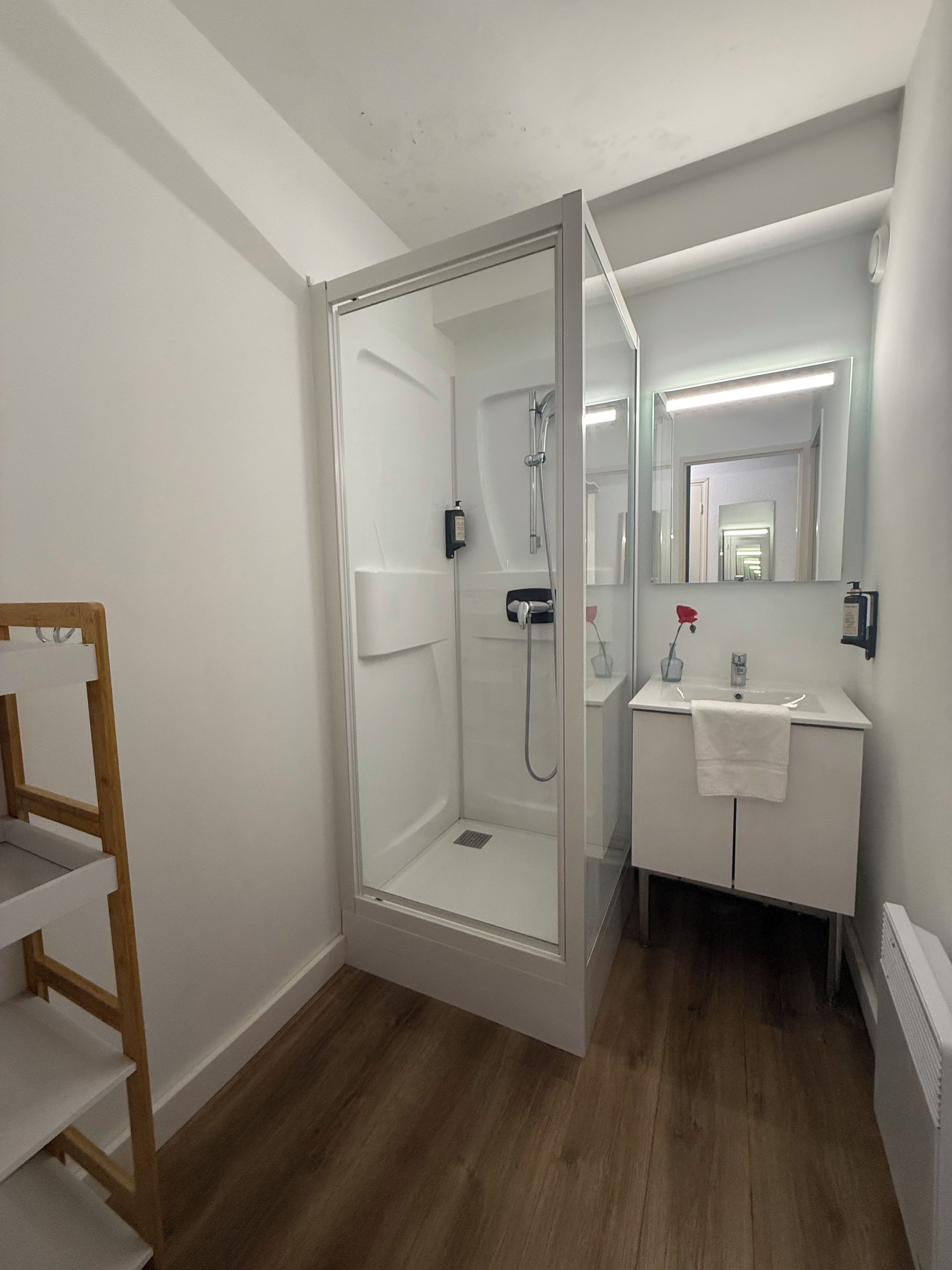 Een moderne badkamer met een douche met glazen wand, een witte wastafel met spiegel en een houten schapunit.