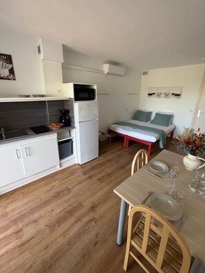 A compact kitchen with a microwave, coffee maker, and a small refrigerator. There is a dining area with a table, chairs, and a vase with flowers. - Résidence Agathéa (Agde)
