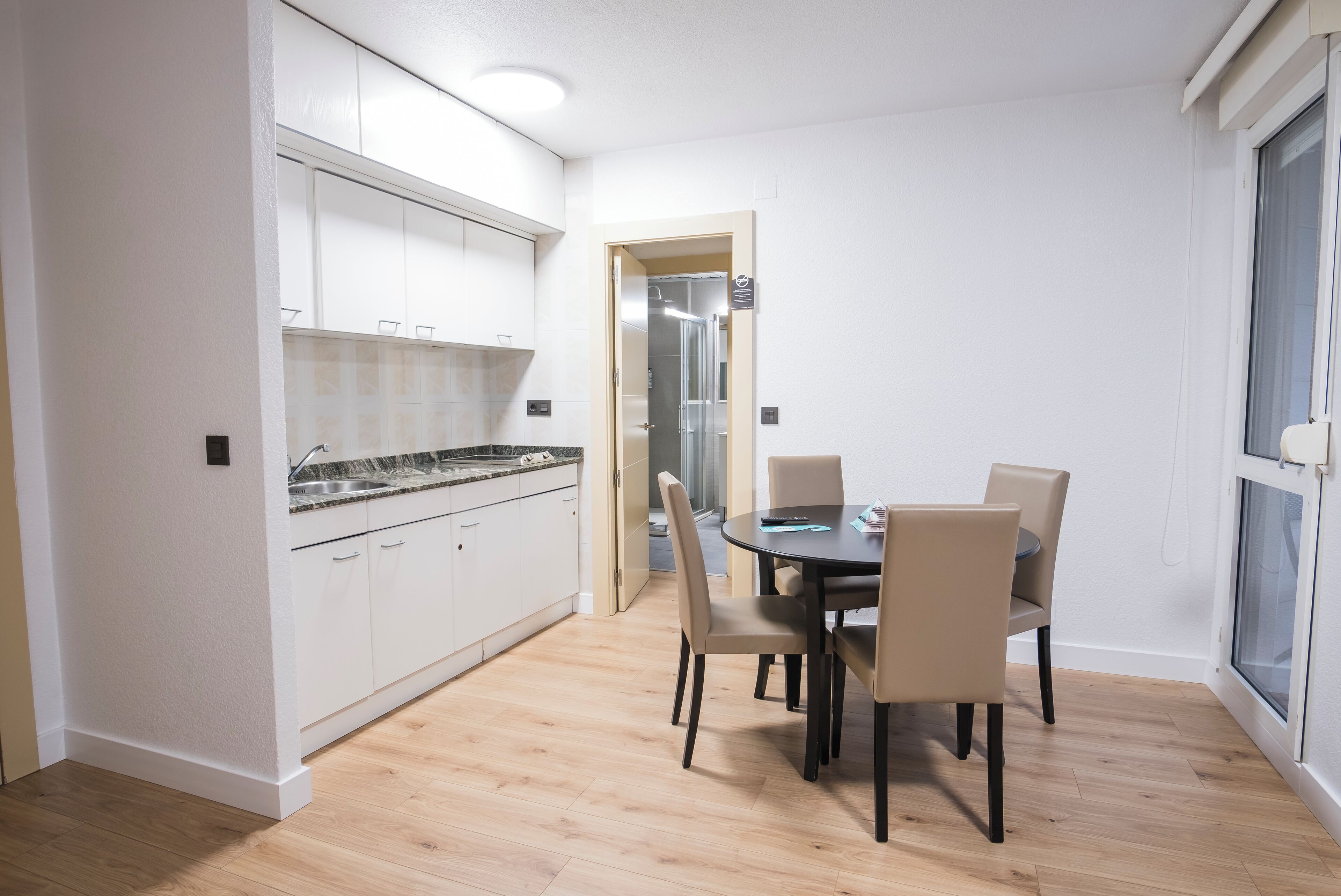 Cocina moderna con armarios blancos y una zona de comedor con una mesa y sillas.