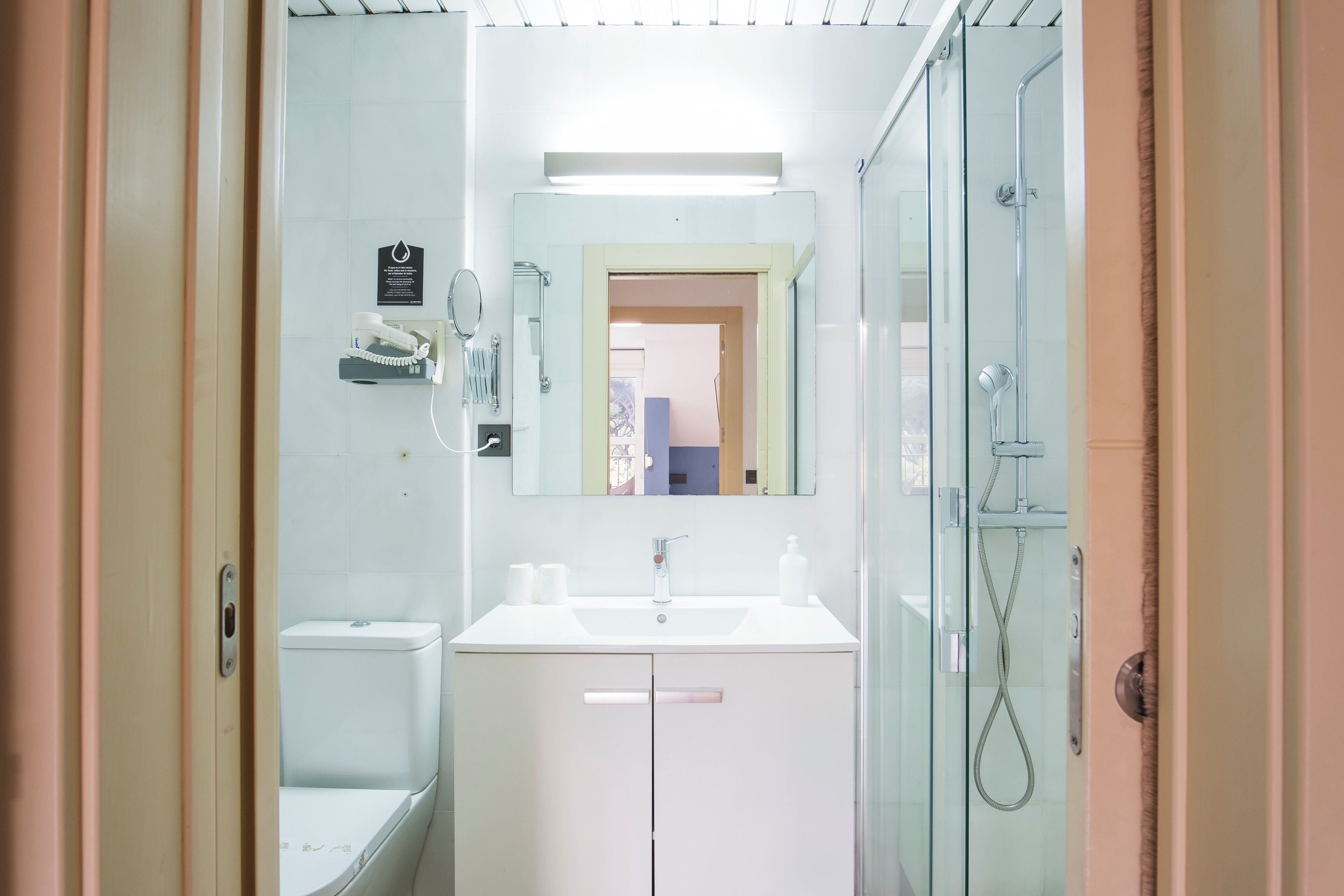 Un baño moderno con lavamanos blanco, espejo y cabina de ducha de vidrio.
