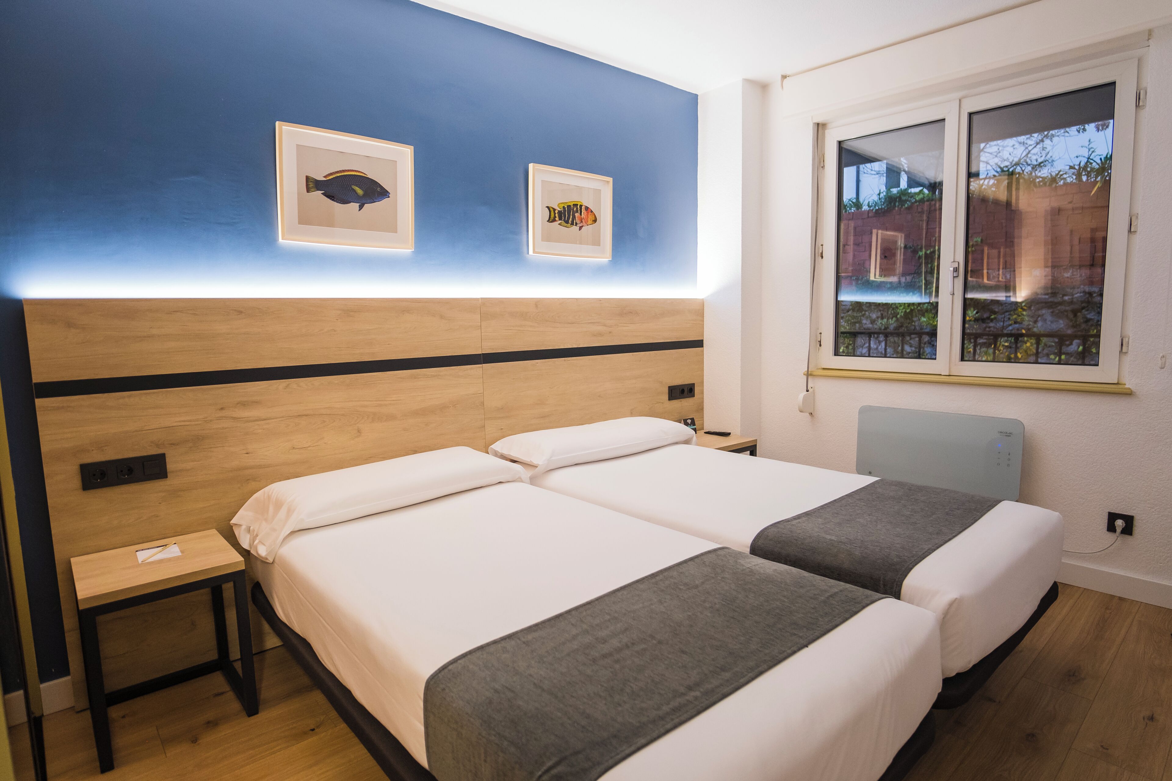 Habitación de hotel con dos camas, una mesita de noche y una ventana con vistas al exterior.