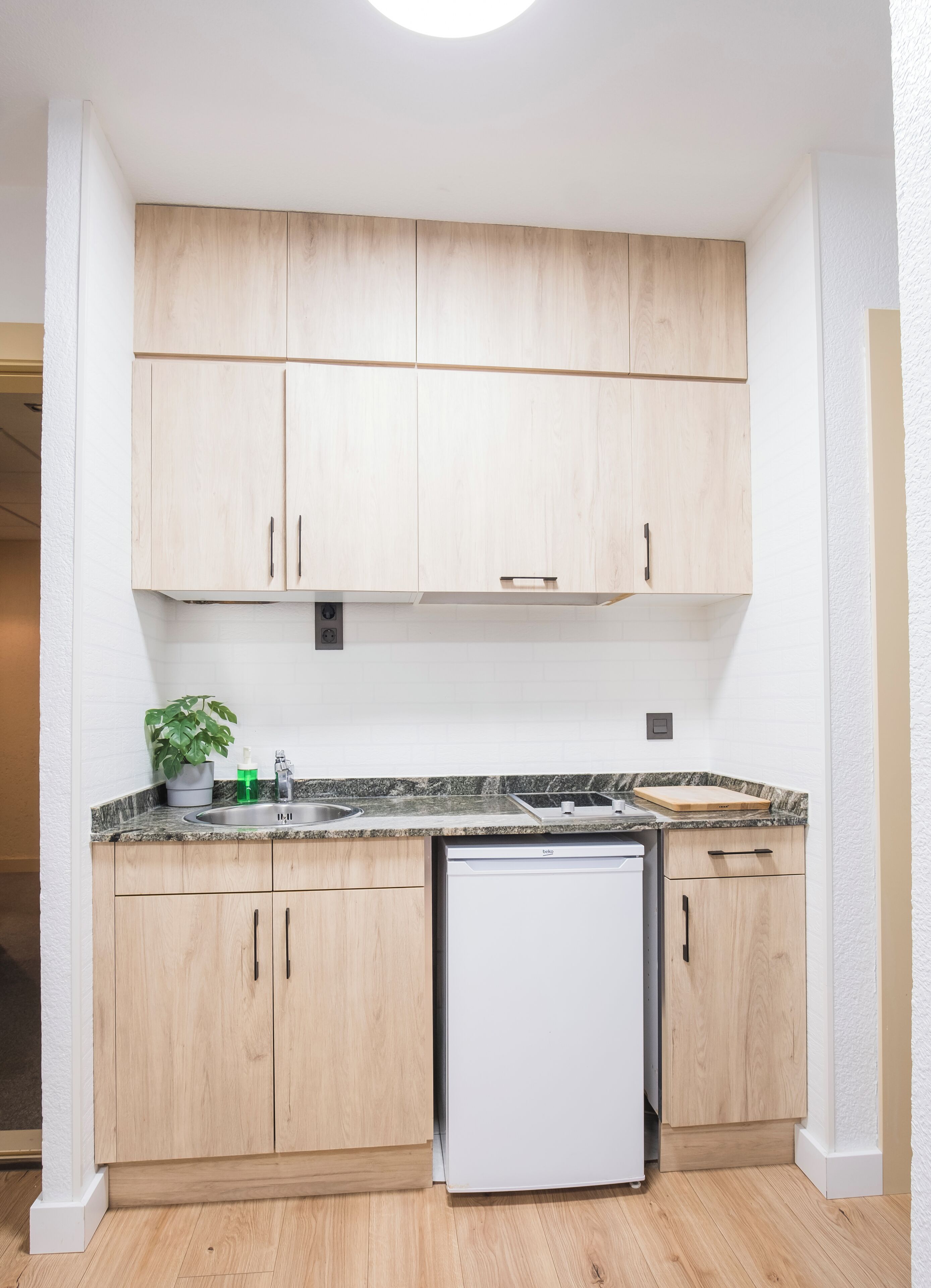 A compact kitchen with wooden cabinets, a built-in dishwasher, and a granite countertop.