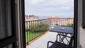 Un balcone con tavolo e sedie, vista su un prato verde e edifici sullo sfondo.