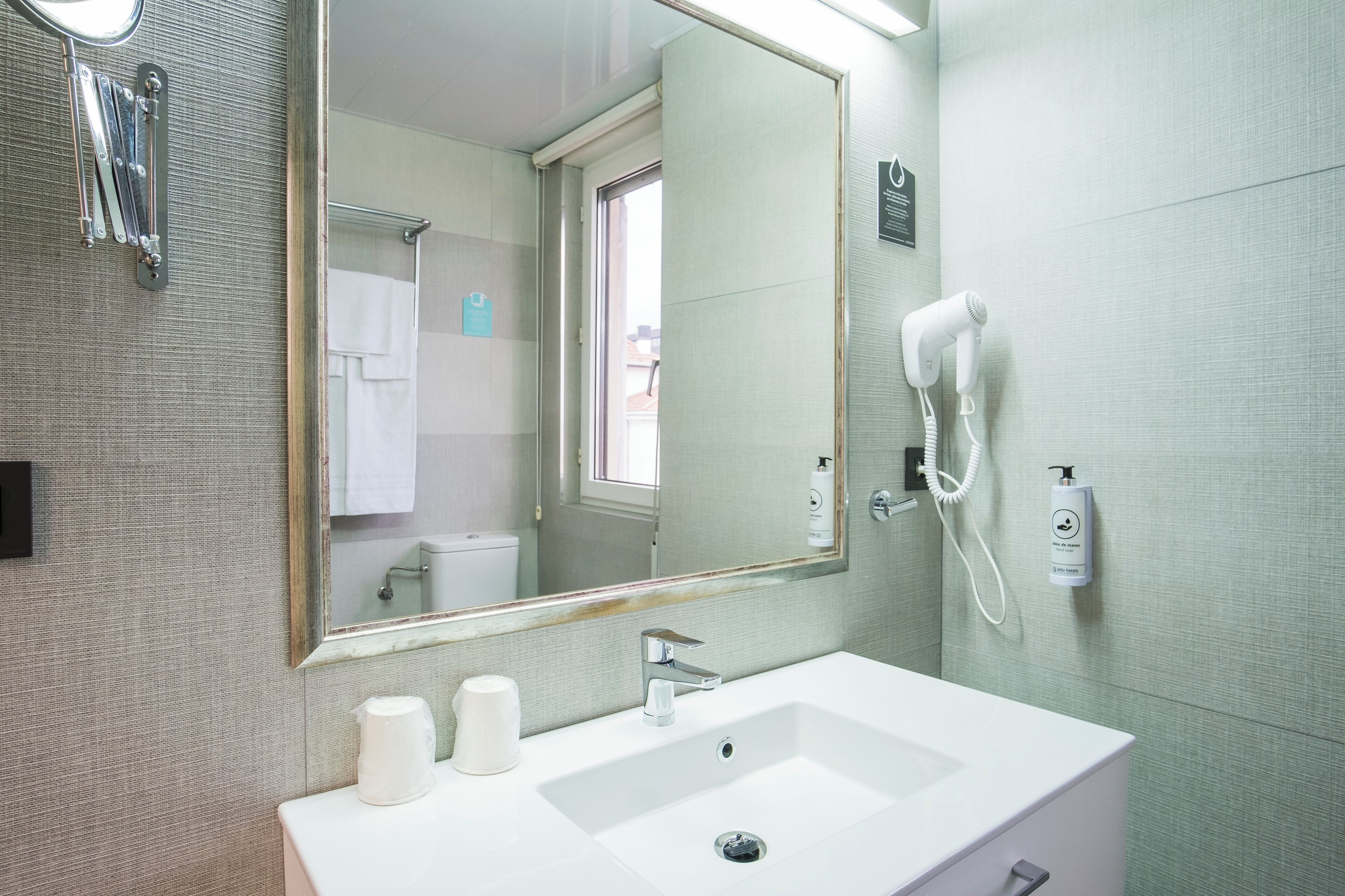 Un baño con un espejo grande, un lavamanos, un secador de pelo y un perchero para toallas.