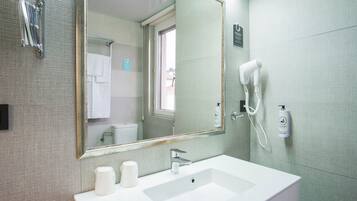 Un baño con un espejo grande, un lavamanos, un secador de pelo y un perchero para toallas.