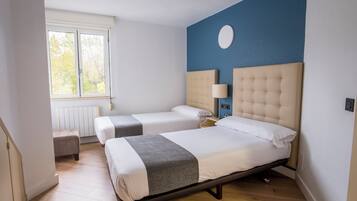 A hotel room with two beds, a window, a radiator, and a blue accent wall.