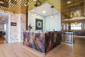 A reception area with a marble wall, a glass counter, and a tropical leaf pattern on the wall. - Alda Don Carlos (Santander)