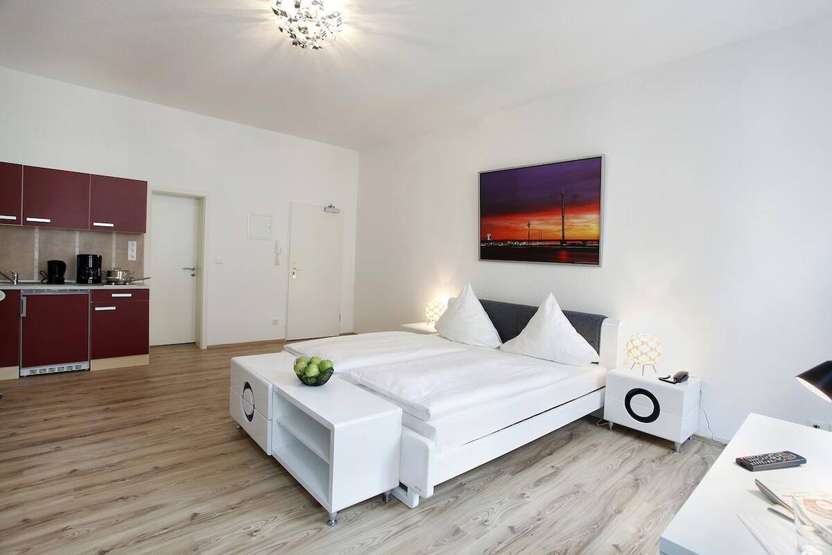 A modern bedroom with a bed, bedside table, and a painting of a sunset.