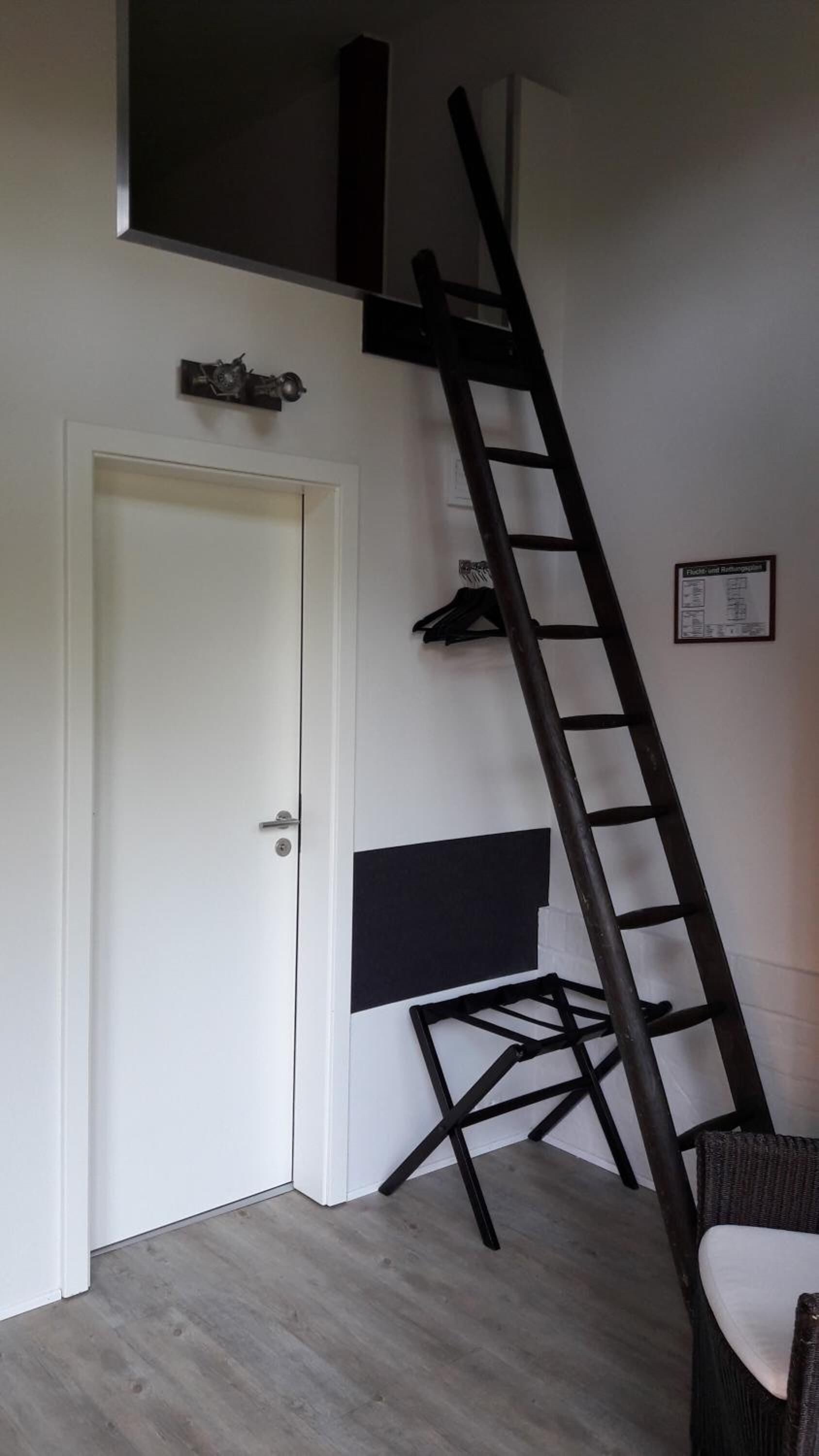 A room with a white door, a black ladder, and a black shelf unit against the wall.