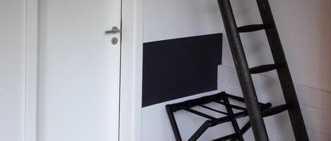 A room with a white door, a black ladder, and a black shelf unit against the wall.