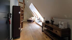 Un dormitorio tipo loft moderno con techo inclinado, piso de madera, armario empotrado, una pequeña cocina americana y vista al área de estar.