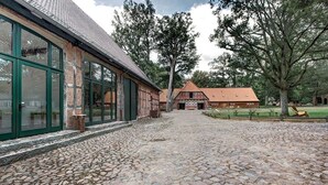 Un patio empedrado con edificios tradicionales, ventanas amplias y un área verde con mesas de picnic.