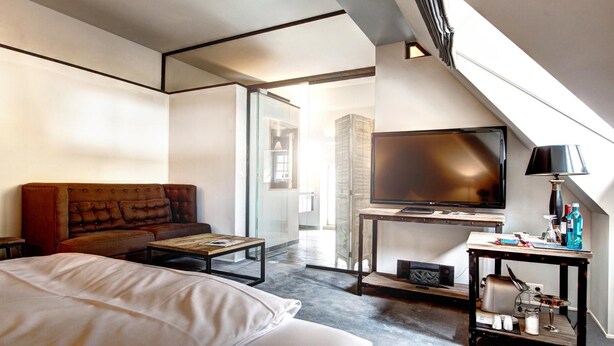 Una habitación de hotel moderna con una cama grande, un sofá de cuero, un televisor y una mesita con artículos de aseo.